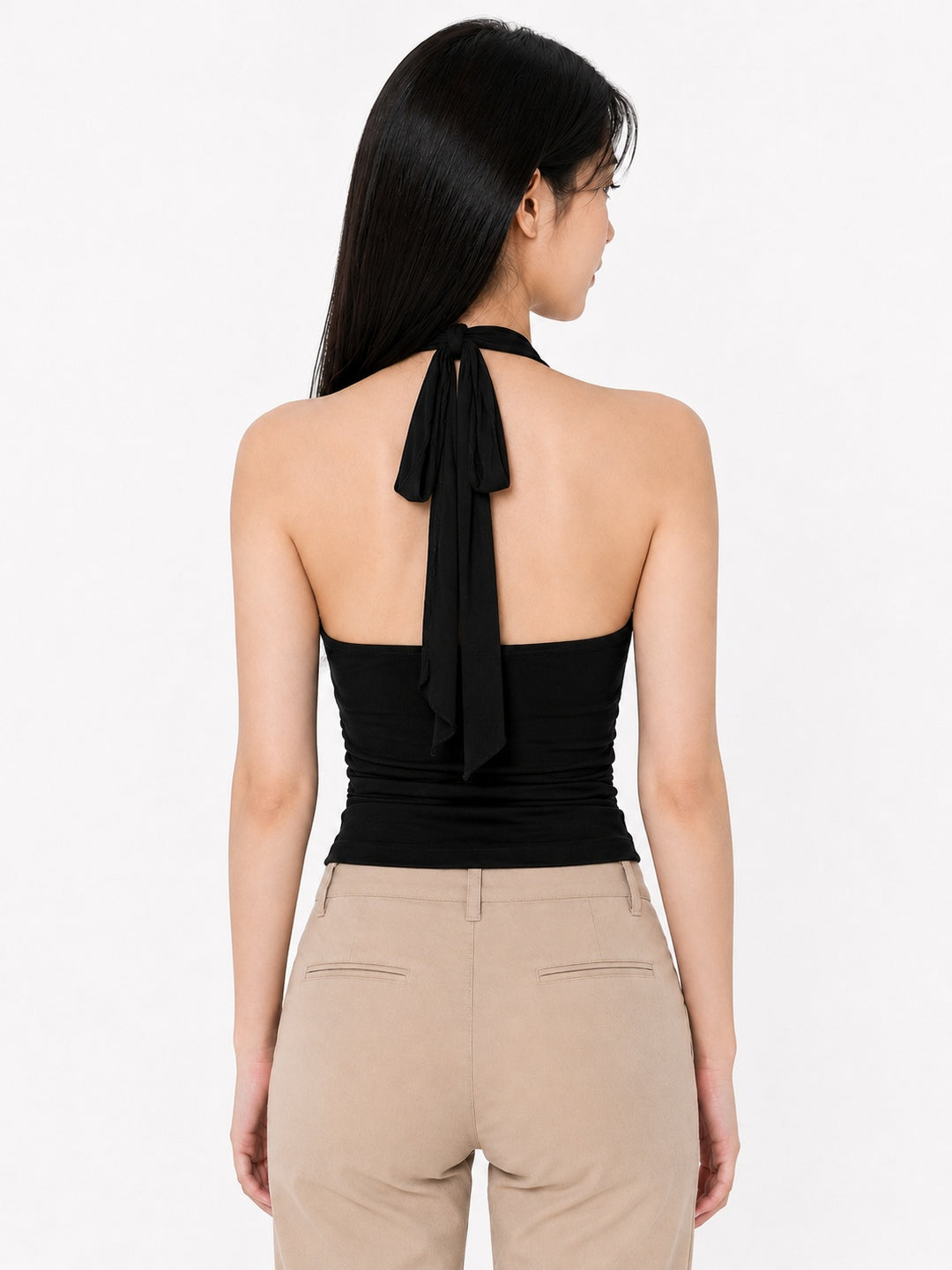 A woman shown from the back wearing a black halter-style top with a long tie at the neck and beige pants, against a plain light background.