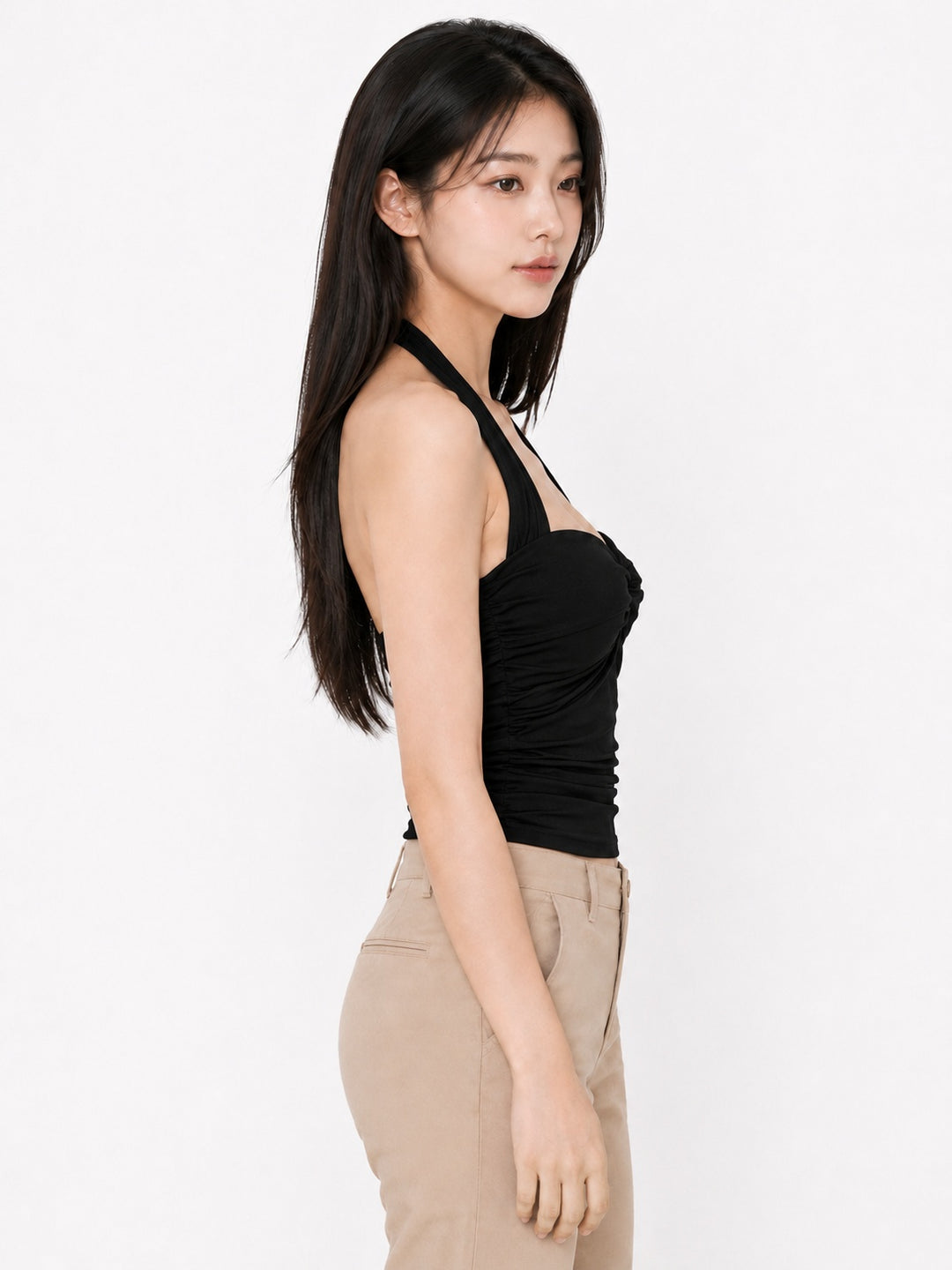A woman shown in side profile wearing a black halter-style ruched tank top and beige pants against a plain light background.