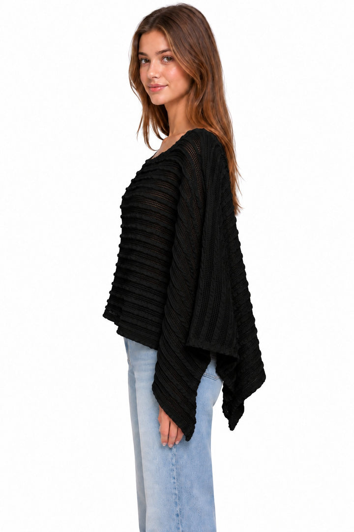 A woman modeling a black textured, wide-sleeved poncho-style top with pleated detailing, paired with light blue jeans, against a plain white background.