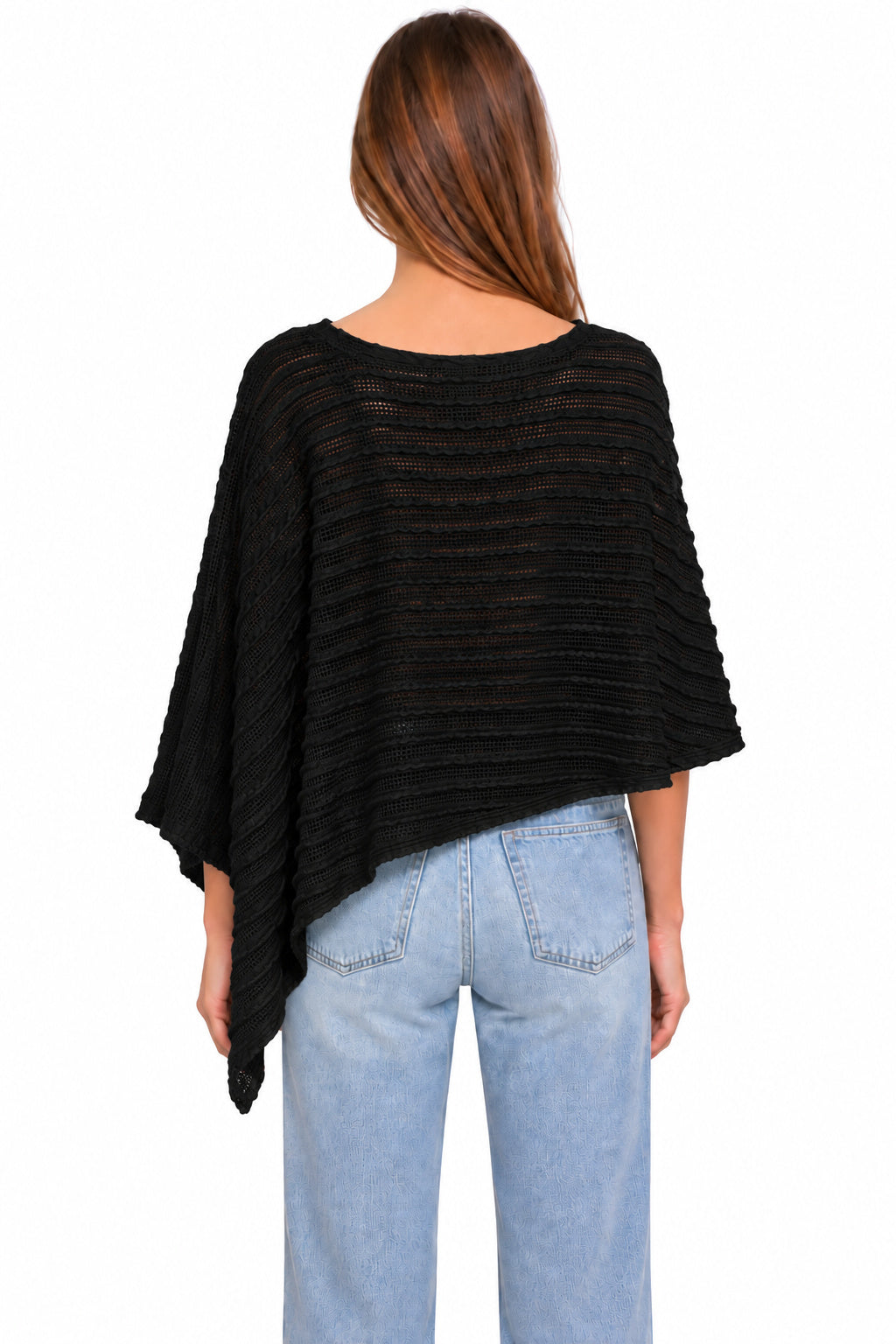 A woman viewed from the back wearing a black textured, semi-sheer poncho-style top and light blue jeans against a plain white background.