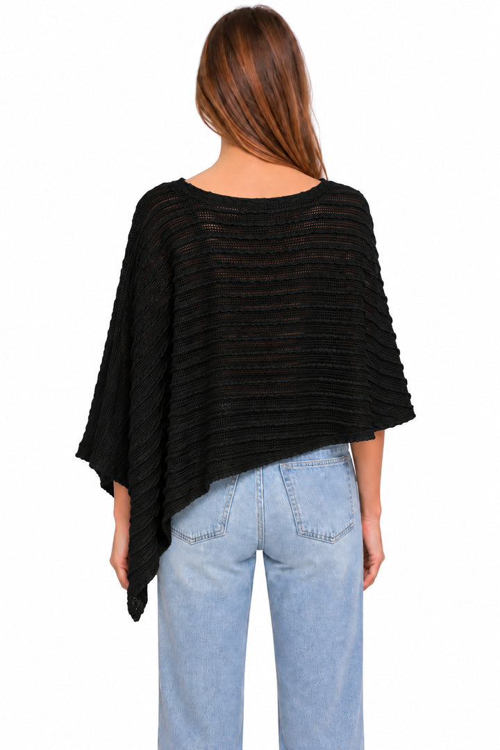 A woman viewed from the back wearing a black textured, semi-sheer poncho-style top and light blue jeans against a plain white background.