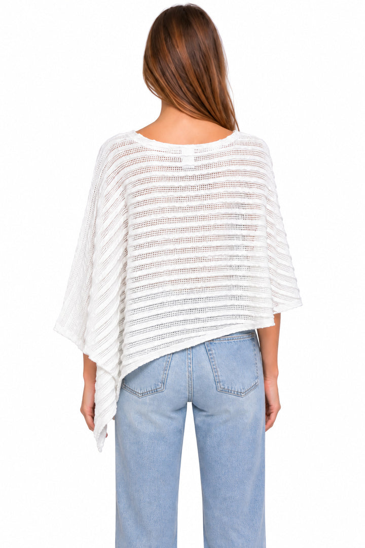 A woman viewed from the back wearing a loose white textured top with wide draped sleeves and light blue jeans, against a plain white studio background.