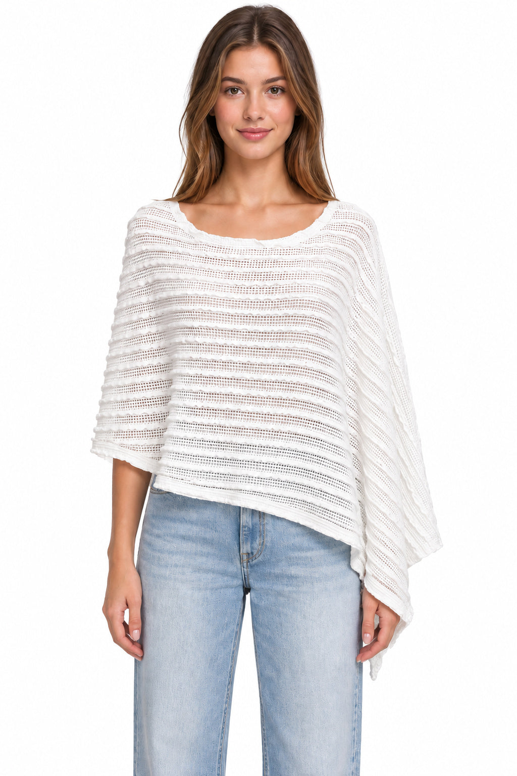 A woman modeling a white textured knit poncho top with wide three-quarter sleeves and an asymmetrical hem, paired with light-wash blue jeans against a plain white background.