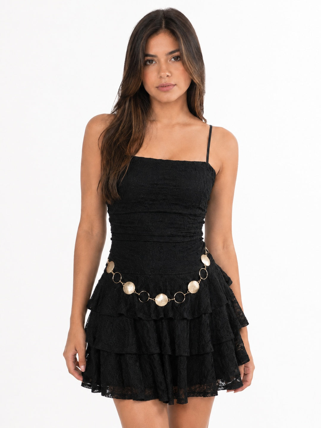 A woman modeling a black tiered mini dress with thin spaghetti straps and a decorative waist accessory featuring gold-tone rings and cream-colored oval charms, set against a plain white studio background.
