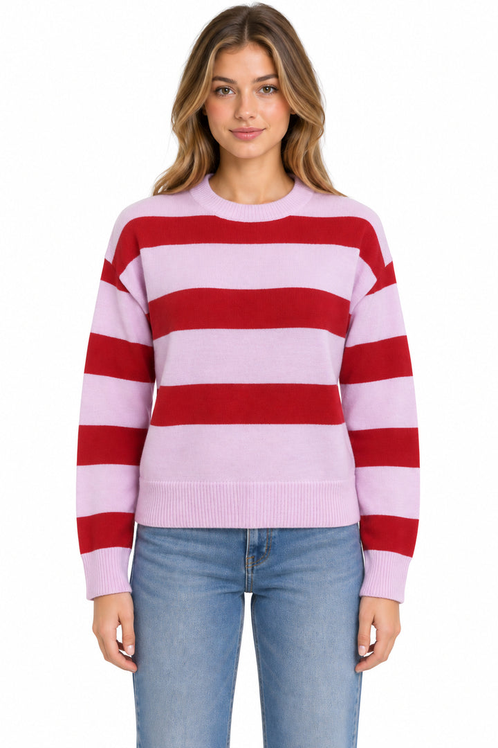 A woman wearing a light pink and red horizontally striped crewneck sweater with light blue jeans, photographed against a plain white background.